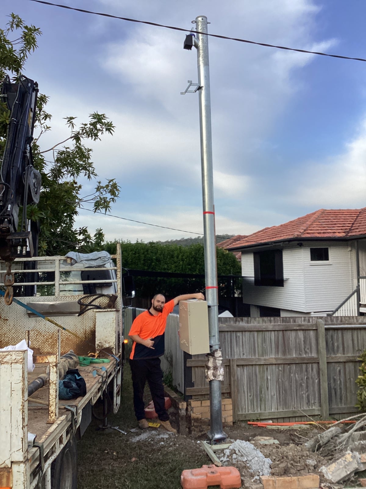 A galvanised permanent power pole standing at full height beside the Poles and Holes crane truck, with the meter box mounted and the crew on site