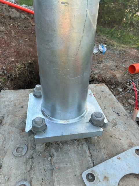 Close-up of a galvanised permanent power pole bolted down to its concrete footing through a base plate and cast-in bolts