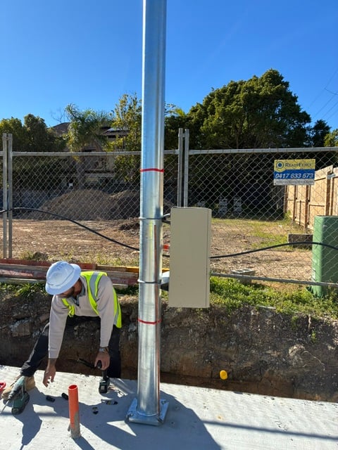 A licensed electrician connecting the underground supply at the base of a galvanised permanent power pole