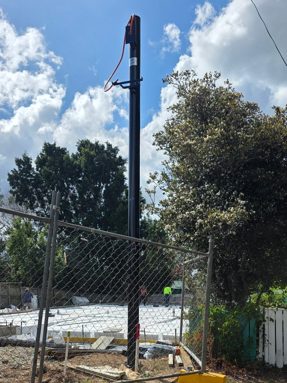 Powder-coated permanent power pole standing on a fenced Brisbane site