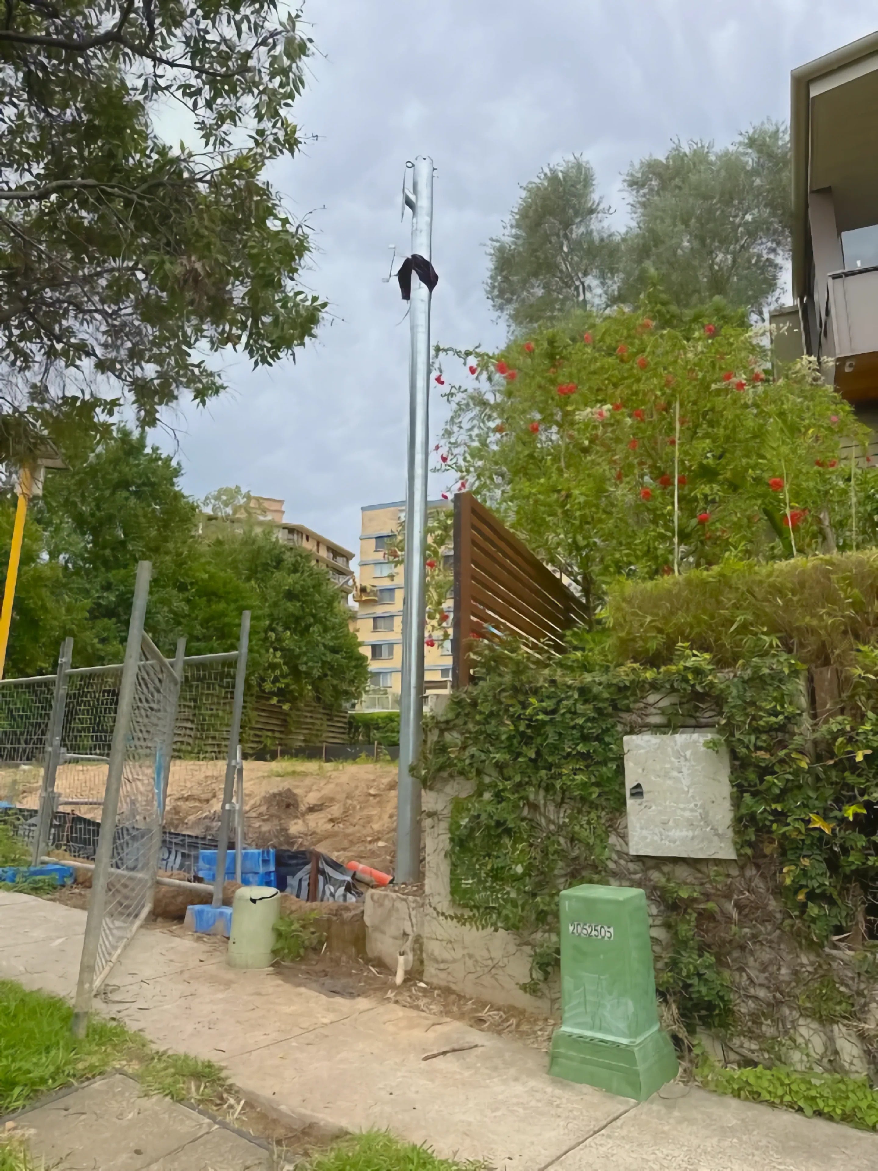 A galvanised permanent power pole installed on the verge of a residential property, beside the site's temporary fencing